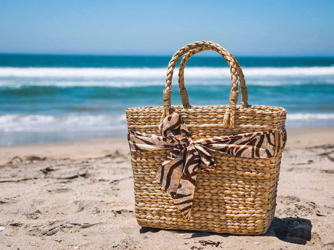 Woven beach tote bag on the sand with the ocean behind it